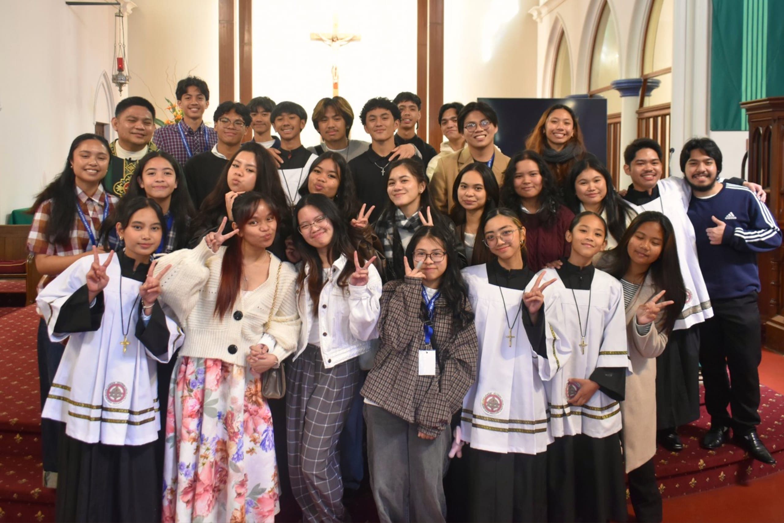 A large group of young people and altar servers smiling together inside the church